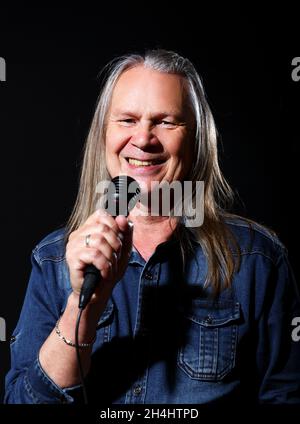 Älterer Mann mit langen grauen Haaren in blauem Denim-Hemd singt auf schwarzem Hintergrund in ein Mikrofon auf der Bühne Stockfoto
