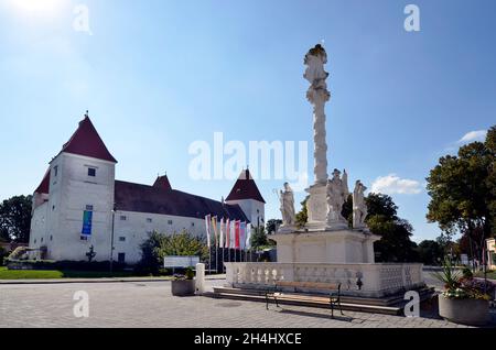 Orth an der Donau, Österreich - 04. September 2021: Dreifaltigkeitssäule und Schloss Orth in Niederösterreich, ehemaliges Wasserschloss, das heute als Museum und Schloss genutzt wird Stockfoto