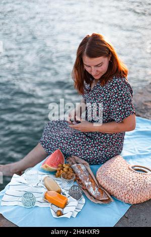 Glückliche Frau mit Essen auf einem Pier, Picknick, Dekor, Hipster. Urlaubskonzept Stockfoto