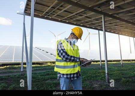 Junger Mann, der mit einem digitalen Tablet am Windpark für erneuerbare Energien arbeitet – Fokus auf Gesicht Stockfoto