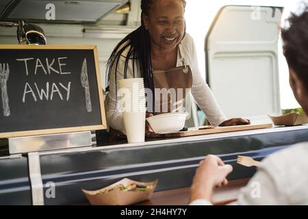 African american Senior Woman serving take away Food inside Food Truck - Weiche Konzentration auf weibliche Gesicht Stockfoto