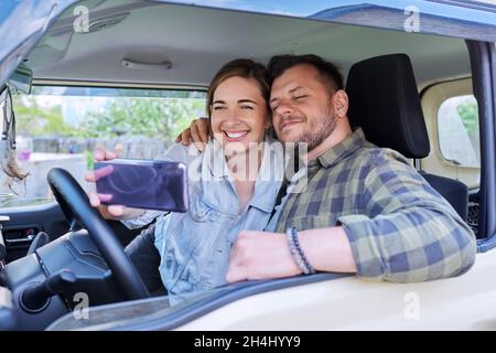 Glückliches Ehepaar, das Selfie-Fotos auf dem Smartphone macht, Ehemann und Ehefrau sitzen im Auto Stockfoto