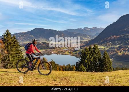 Nette Frau mit Elektro-Mountainbike genießt den Blick über den Alpsee in atumnaler Atmosphäre in den allgäuer alpen oberhalb von Immenstadt, Bayerische Alm Stockfoto