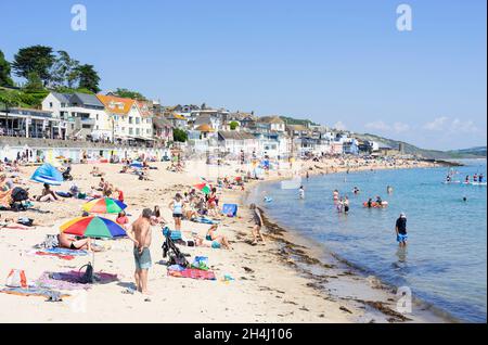 Familien am Strand mit Pop-up-Strandzelten Liegestühle Sonnenschirme und Paddle-Boards am Sandstrand bei Lyme Regis Dorset England GB Europa Stockfoto