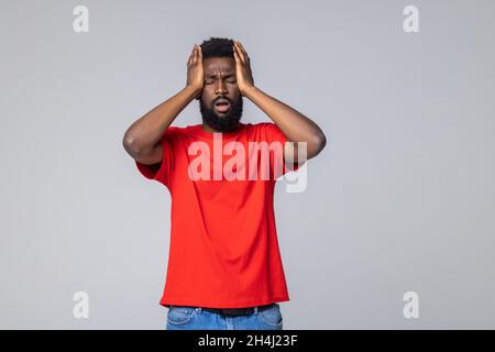 Zweifel, denken müssen. Bärtiger Mann mit Dreadlocks-Händen am Kopf, während er mit verwirrtem, rätselhaftem Gesicht auf grauem Hintergrund denkt. Stockfoto