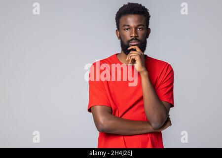 Dunkelhäutiger junger Mann mit weißem Sweatshirt, der auf grauem Hintergrund steht und eine Idee denkt Stockfoto