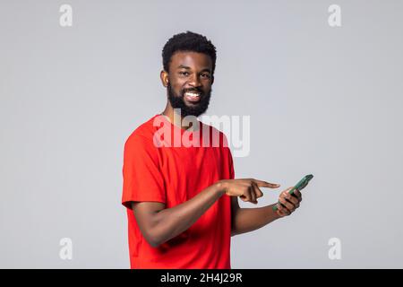 Junger afroamerikanischer Mann auf grauem Hintergrund, SMS schreiben oder mit einem glücklichen, entspannten Lächeln surfen Stockfoto