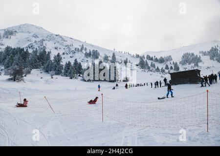 Skifahrer und Kinder, die auf einer verschneiten Skipiste im Schlitten fahren, genießen Winterurlaub im Kalavryta Ski Resort in Griechenland Stockfoto