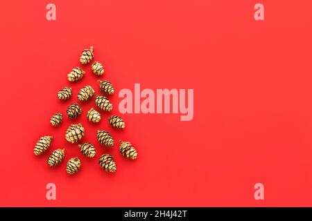 Neujahrs- und Weihnachtskarte. Abstrakter Weihnachtsbaum aus goldenen Zapfen auf hellrotem Hintergrund. Minimales Weihnachtskonzept. Draufsicht, Kopierer-SPAC Stockfoto