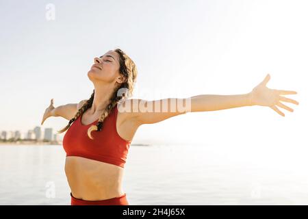 Lächelnde Erwachsene Frau atmet tiefe frische Luft und streckt die Arme am Strand aus Stockfoto