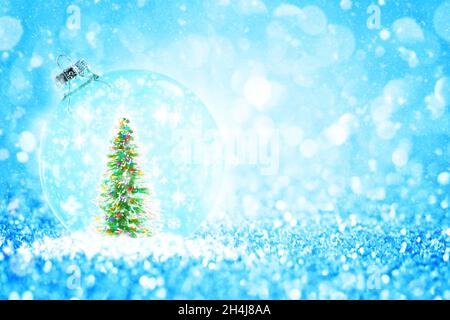 Transparente Kugel mit grünen bunten Glitter Kiefer Weihnachtsbaum unter Schneeflocken vor glitzernden hellblauen Hintergrund. Stockfoto