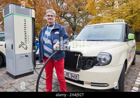 Hamburg, Deutschland. November 2021. Birgits Neumann, Taxifahrerin, steht mit ihrem Hybrid London Taxi bei der Eröffnung des ersten vollelektrischen Taxistandes Hamburgs neben einer Ladestation. Der Taxistand ist mit einer leistungsstarken Ladestation ausgestattet. Quelle: Georg Wendt/dpa/Alamy Live News Stockfoto