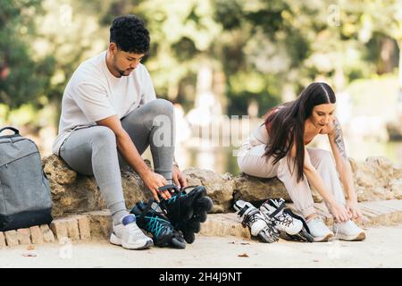 Junges Paar, das auf einem Park sitzt und auf Inline-Skates padelt Stockfoto