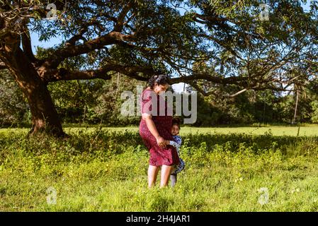 Indische Familie von Mutter und Kleinkind in einem Garten und in Erwartung eines zweiten Kindes Stockfoto