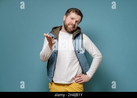 Wohlwollender Mann weist anklagend auf jemanden mit der Hand hin und lächelt freundlich. Blauer Hintergrund. Stockfoto