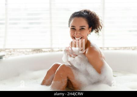 Porträt einer lächelnden, mit Schaumstoff überzogenen Frau, die zu Hause in einem heißen Schaumbad sitzt und Platz kopiert Stockfoto