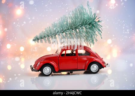 Auto mit einem Weihnachtsbaum auf einem festlichen Hintergrund. Frohe Weihnachten und ein glückliches neues Jahr Postkarte. Stockfoto