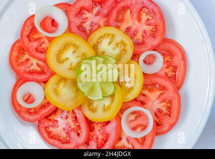 Tomatensalat mit Zwiebelringen garniert und ein Stück von Kalk. Stockfoto