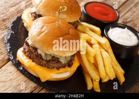 Amerikanische Butterburger mit Rindfleisch, Zwiebeln und Käse, serviert mit Pommes und Saucen aus nächster Nähe auf dem Tisch. Horizontal Stockfoto