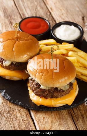 Butterburger mit Rindfleisch, Zwiebeln und Cheddar-Käse, serviert mit Pommes und Saucen aus nächster Nähe auf einem Schiefertafel auf dem Tisch. Vertikal Stockfoto