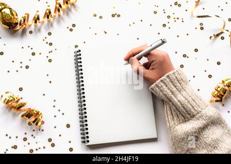 Frauenhand mit Schreibfeder im Notizbuch auf weißem Tisch mit Weihnachtsschmuck. Draufsicht, flach liegend. Modell. Stockfoto