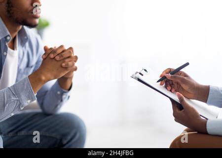 Nicht erkennbarer Psychologe, der depressiven männlichen Patienten unterstützt, in der Arztpraxis auf der Zwischenablage schreibt, Nahaufnahme Stockfoto