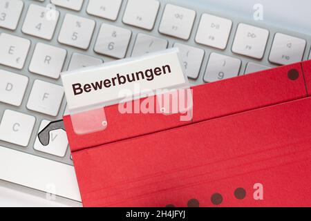 Das deutsche Wort für Bewerbungen ist auf dem Etikett einer roten Hängemappe zu sehen. Der Hängeordner befindet sich auf einer Computertastatur. Stockfoto