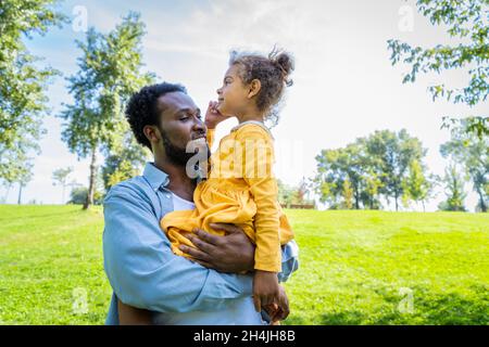Schöne glückliche afroamerikanische Familie, die sich im Park festmacht - Schwarze Familie, die Spaß im Freien hat, Papa, der mit seiner niedlichen Tochter spielt Stockfoto