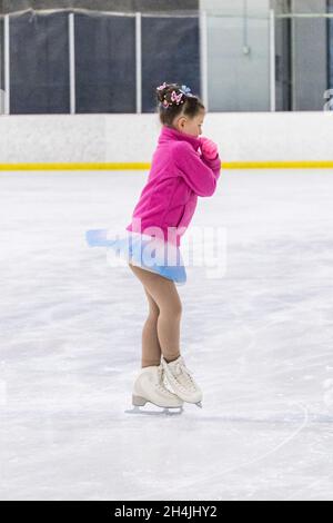 Kleines Mädchen, das Eiskunstlauf auf einer Indoor-Eisbahn übt. Stockfoto