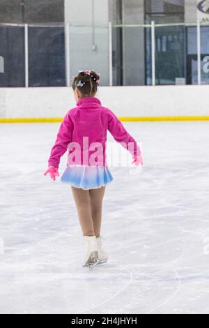 Kleines Mädchen, das Eiskunstlauf auf einer Indoor-Eisbahn übt. Stockfoto