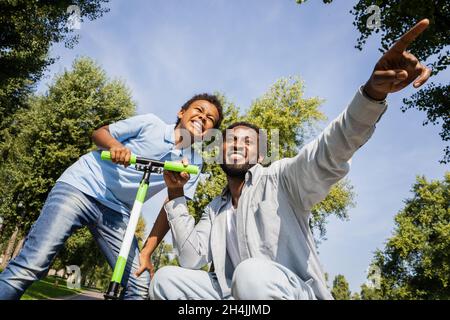 Schöne glückliche afroamerikanische Familie im Park - Schwarze Familie, die Spaß im Freien hat, Vater, der Sohn lehrt, auf dem Roller zu fahren Stockfoto