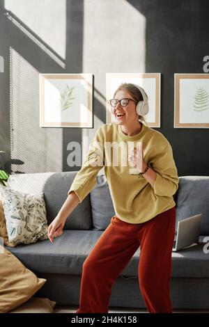 Glückliche junge Frau, die Musik in Kopfhörern hört und zu Hause im Zimmer tanzt Stockfoto