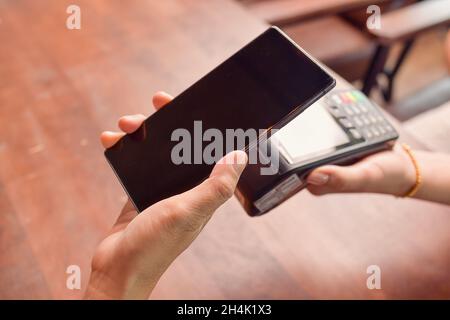 Person, die eine kontaktlose Zahlung mit einem Mobiltelefon auf einem Kreditkartenleser abgibt Stockfoto