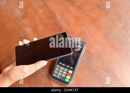 Person, die eine kontaktlose Zahlung mit einem Mobiltelefon auf einem Kreditkartenleser abgibt Stockfoto