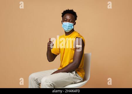 Werbung Für Die Impfung Gegen Coronaviren. Glücklich Geimpfter Schwarzer Kerl Mit Gips Am Arm Zeigt Daumen Nach Oben Nach Bekommen Covid-19-Impfstoff-Injektion, Afric Stockfoto