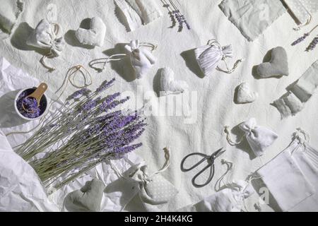 Handgemachte Lavendelsäckchen in Textiltaschen und weichen Herzen. Trockene Lavendelblüten zum Füllen, Scheren und Kerzen. Flacher Lay auf Leinentextilien Stockfoto