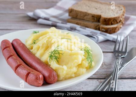 Kartoffelpüree, garniert mit Dill und Würstchen auf einem alten Holzhintergrund. Stockfoto