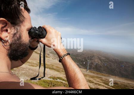 Nahaufnahme eines jungen Mannes, von der Seite gesehen, der mit einem Fernglas die Aussicht anschaut. Stockfoto
