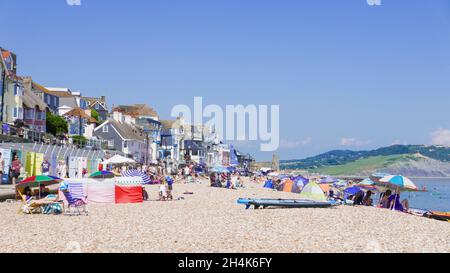 Familien am Strand mit Pop-up-Strandzelten Liegestühle Sonnenschirme und Paddle-Boards am Sandstrand bei Lyme Regis Dorset England GB Europa Stockfoto