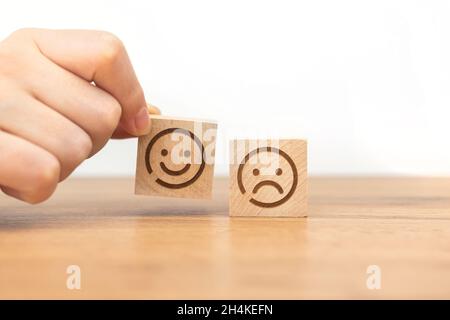 Die Hand des Kunden wählt das Smiley-Gesicht-Symbol auf einem Holzwürfel. Service-Rating, Zufriedenheit und Marketing-Konzept Stockfoto