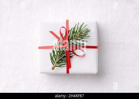 Eine weiße Weihnachts-Geschenkbox mit Tannenzweig auf weißem Leinentischtuch. Stockfoto