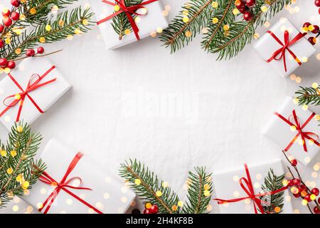 Weihnachtsrahmen aus Geschenkschachteln und Tannenzweigen auf weißer Tischdecke. Stockfoto