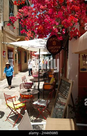 Nafplio - Griechenland - Mai 25 2018 : kleines Straßencafé in einer bunten Straße im Herzen der historischen Altstadt schöne Blumen in einer schattigen Gasse V Stockfoto