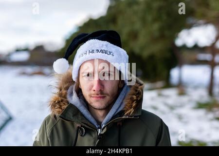 Ein mürrischer junger Mann, der einen schwarzen weihnachtsmann-Hut mit den Worten Bah Humbug trägt