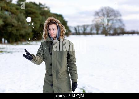 Ein entschlossen aussehender junger Mann mit einem Schneeball in der Hand, der bereit ist, ihn während einer Schneeballschlacht zu werfen. Er ist in einer schneebedeckten winterlichen Landschaft Stockfoto