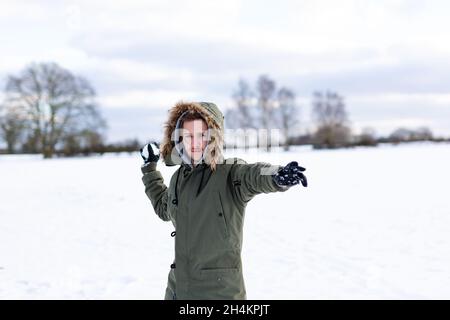 Ein entschlossen aussehender junger Mann mit einem Schneeball in der Hand, der bereit ist, ihn während einer Schneeballschlacht zu werfen. Er ist in einer schneebedeckten winterlichen Landschaft Stockfoto