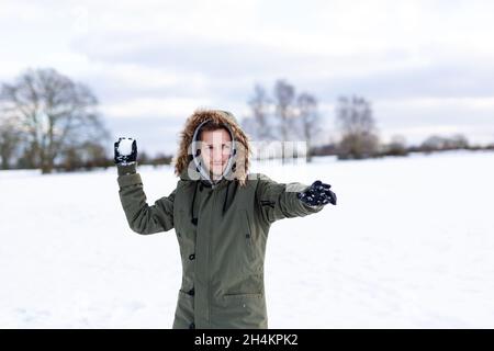 Ein entschlossen aussehender junger Mann mit einem Schneeball in der Hand, der bereit ist, ihn während einer Schneeballschlacht zu werfen. Er ist in einer schneebedeckten winterlichen Landschaft Stockfoto