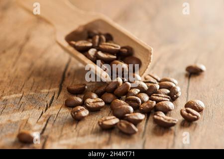 Nahaufnahme von gerösteten Kaffeebohnen mit einem kleinen Holzlöffel auf einer Oberfläche aus altem Holz in horizontaler Ausrichtung bei Blende F7. Stockfoto