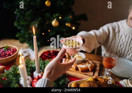 Nahaufnahme von der Seite, in der unerkennbare junge Frau und Mann während der Weihnachtsfeier an einem festlichen Weihnachtstisch sitzen, an dem köstliche Speisen vorbeigehen Stockfoto