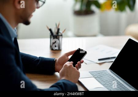 Unkenntlich männlicher Geschäftsmann, der mit Laptop-Computer und Smartphone im Büro arbeitet, Nachbau. Beschnittene Ansicht des arabischen Unternehmers mit modernen Gadgets Stockfoto